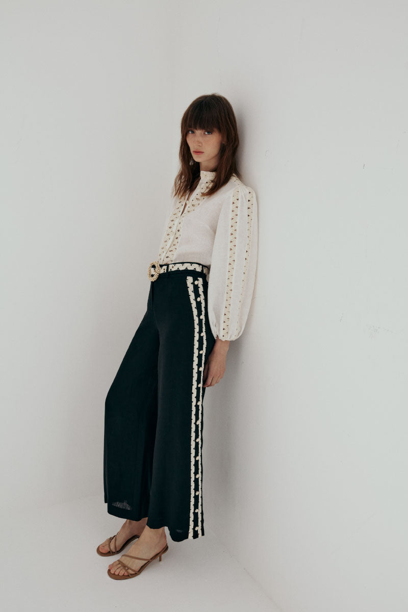 A pair of AISA LEA pants in a neutral color, displayed on a wooden surface with a casual, relaxed fit.