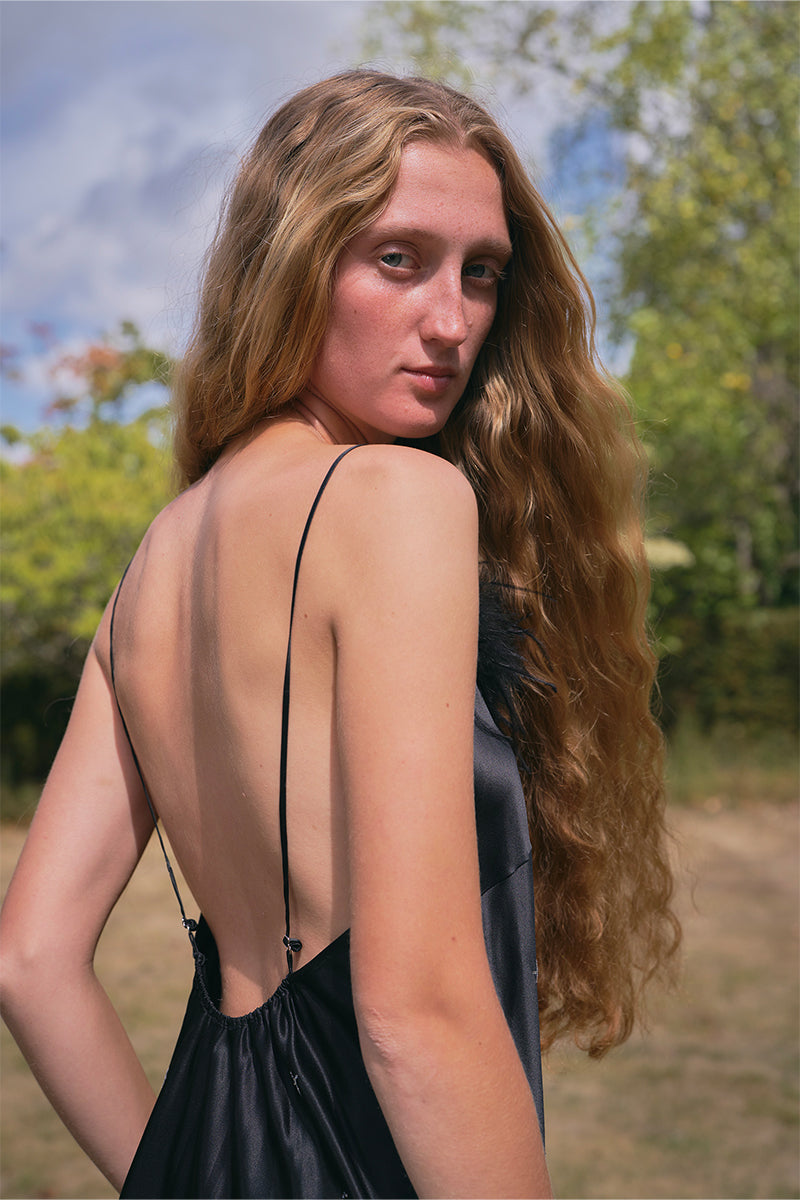 Black bias-cut slip dress with rhinestones and feather embellishments, featuring a flowy maxi dress design by Not Just Pajama.