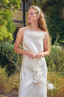 White bias-cut maxi dress with rhinestone embellishments and feather accents, featuring a flowing silhouette and elegant design.