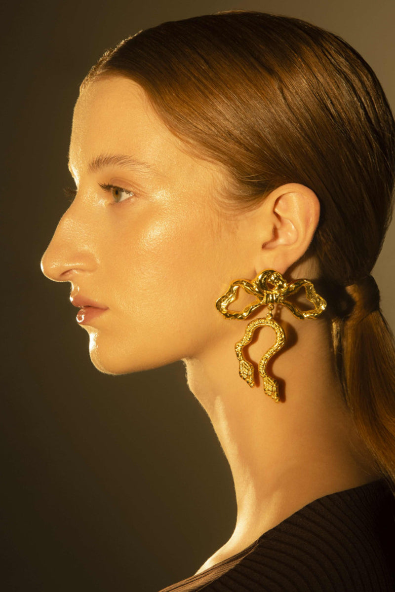 Natia x Lako bow earrings with asymetric snake design, gold-tone metal, and intricate detailing for a stylish look.