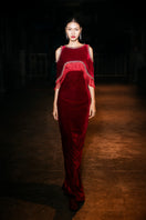 Red Valenciani gown with shoulder cutouts, elegant cape design, flowing fabric, worn by a model in a studio setting.