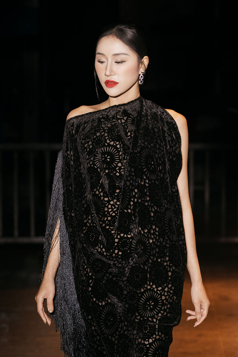 Black Valenciani draped gown with side fringe, elegant design, showcasing flowing fabric and intricate detailing.