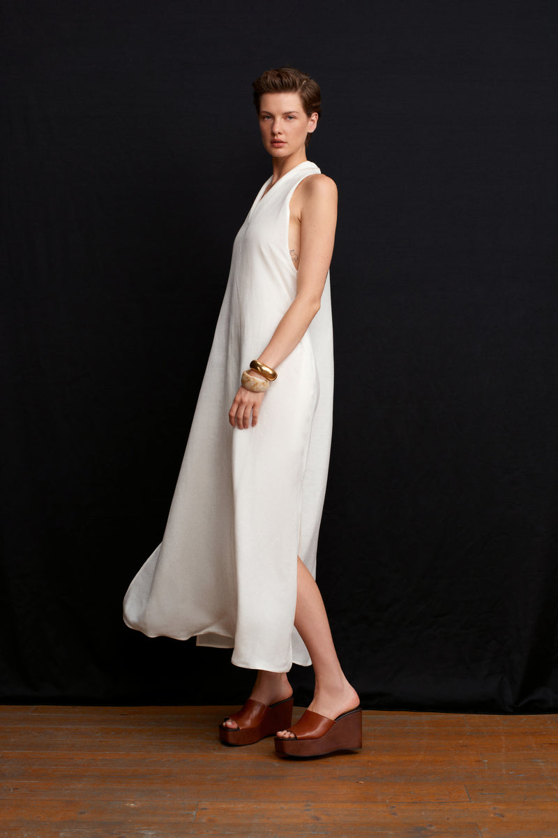 White Acaria Studio La Plage maxi dress displayed on a hanger with flowing fabric and a relaxed beachy style.