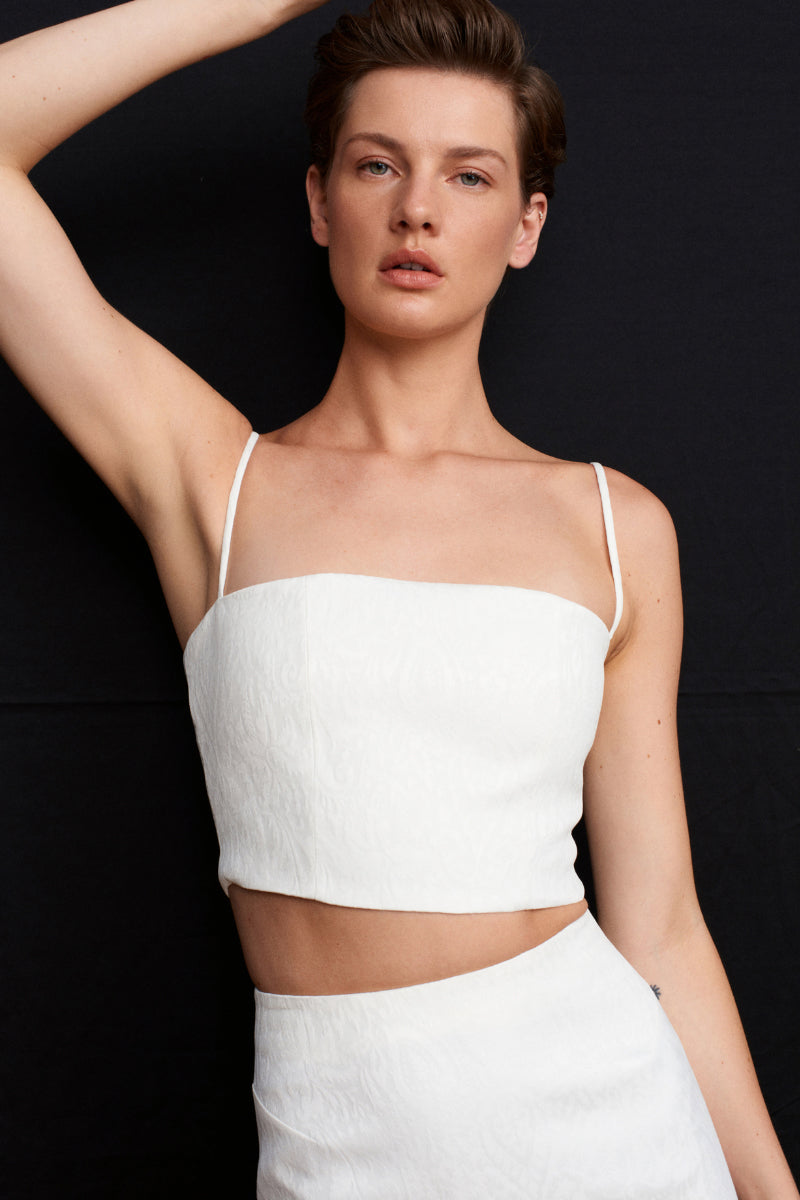 White ancient-inspired top from Acaria Studio featuring intricate detailing and a relaxed fit, ideal for stylish casual wear.