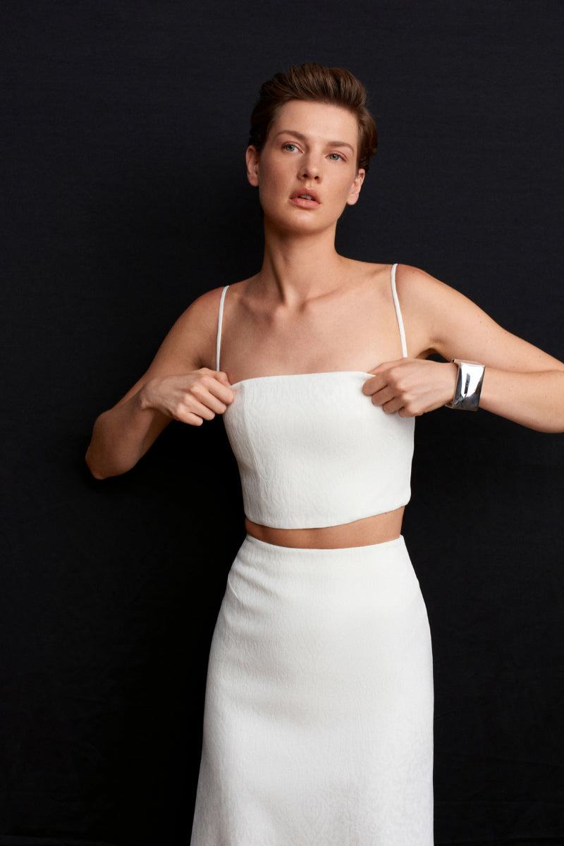 White Ancient Top by Acaria Studio featuring a relaxed fit and elegant design, displayed on a hanger.