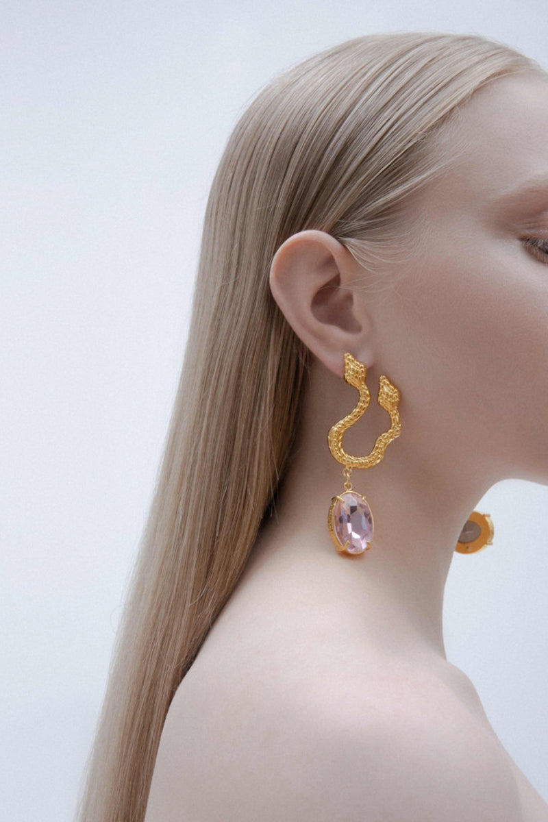 Asymmetric snake earrings by Natia x Lako featuring light pink crystal accents and gold-tone details.