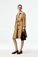 Beige cotton trench coat by Chictopia, featuring classic double-breasted design and belt, styled for a sophisticated look.