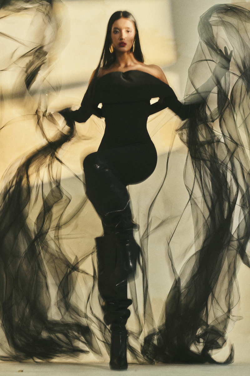 L'SCARLETT form-fitting off-shoulder long-sleeve poly crepe jumpsuit displayed on a model, showcasing its sleek design.