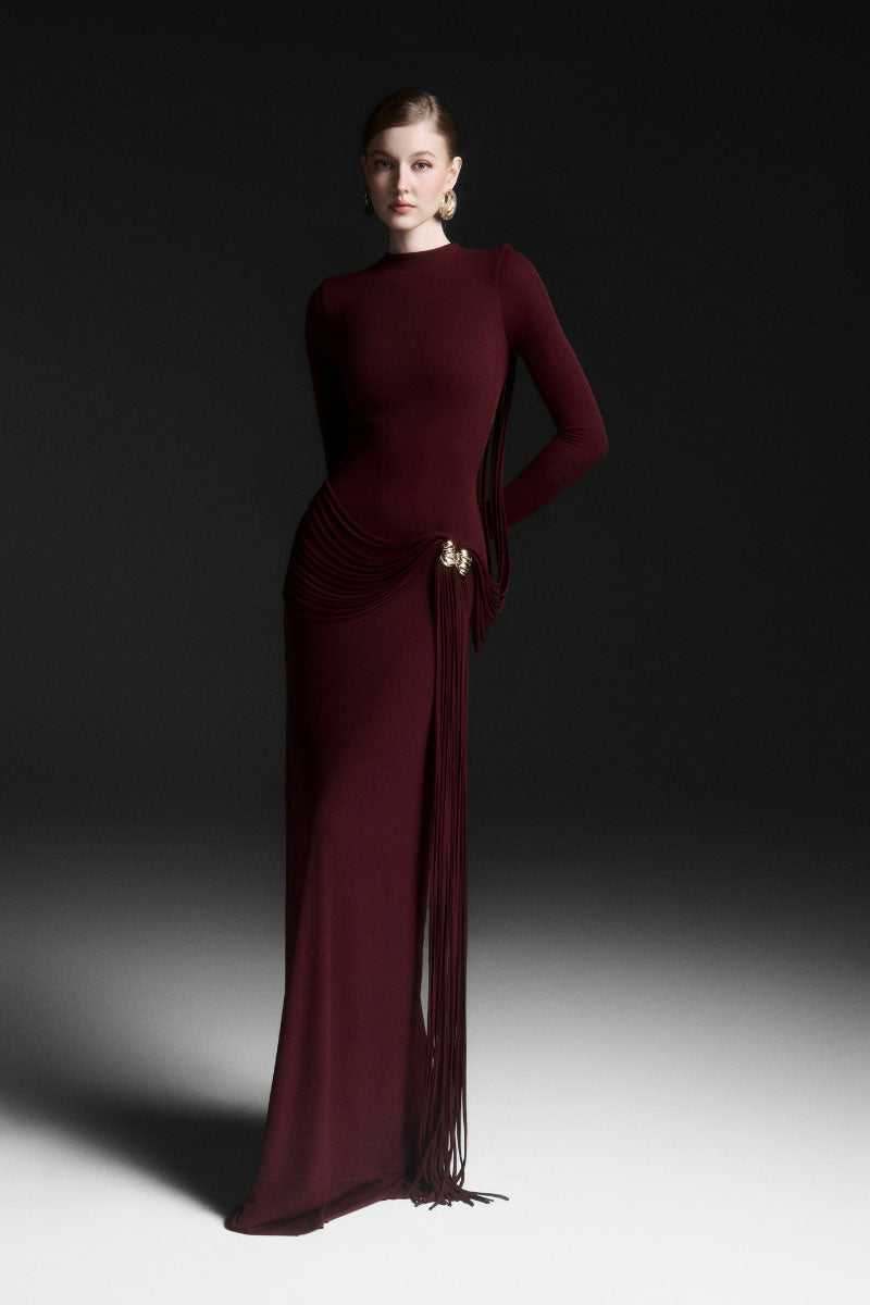 Red Maison Des Copains Corvina draped floor-length maxi dress displayed on a mannequin with flowing fabric and elegant design.