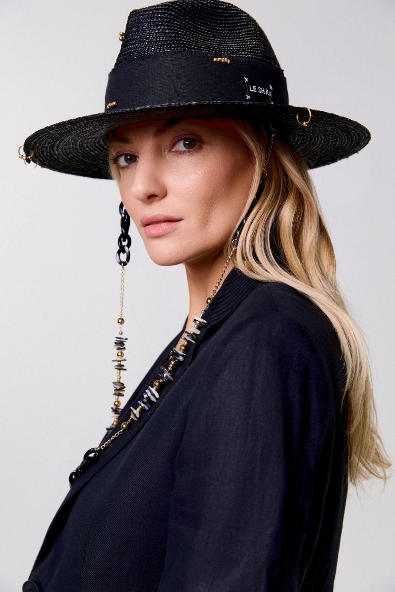 Black fedora hat by LE SH KA with shell embellishments and 24K gold-plated accessories, featuring a stylish wide brim and decorative details.