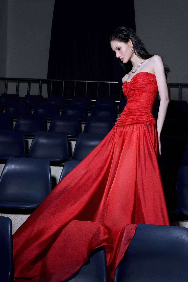 Red draped corset gown by CEM featuring a flowing silhouette and elegant fabric, perfect for formal occasions.