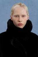 Black oversized shearling coat by JINSUN, featuring plush shearling lining and a relaxed fit, displayed hanging on a wooden background.