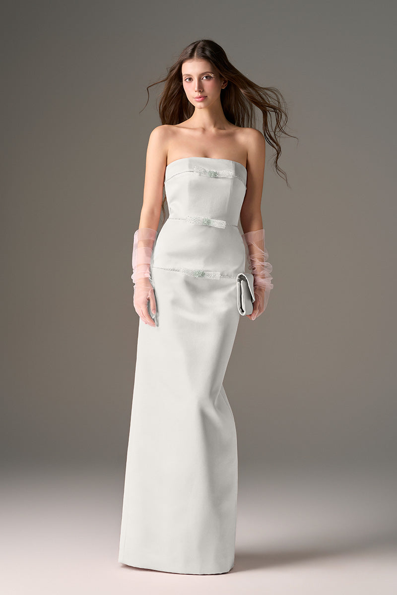 Light gray CULT MIA X I.H.F Studio taffeta column gown displayed on a dress form with elegant draping and fitted silhouette.
