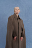 Brown long wool cape coat by JINSUN hanging on a rack, showcasing its elegant, flowing design and textured fabric.