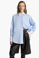 Acaria Studio iconic French blue shirt displayed on a hanger, featuring a classic collar and button-down front.