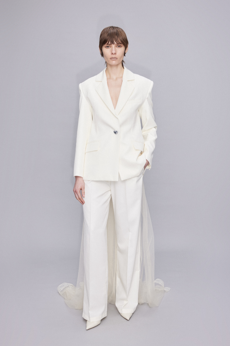 Light-colored low waist straight-cut pants in ecru from Sudi Etuz, shown hanging on a wooden hanger.