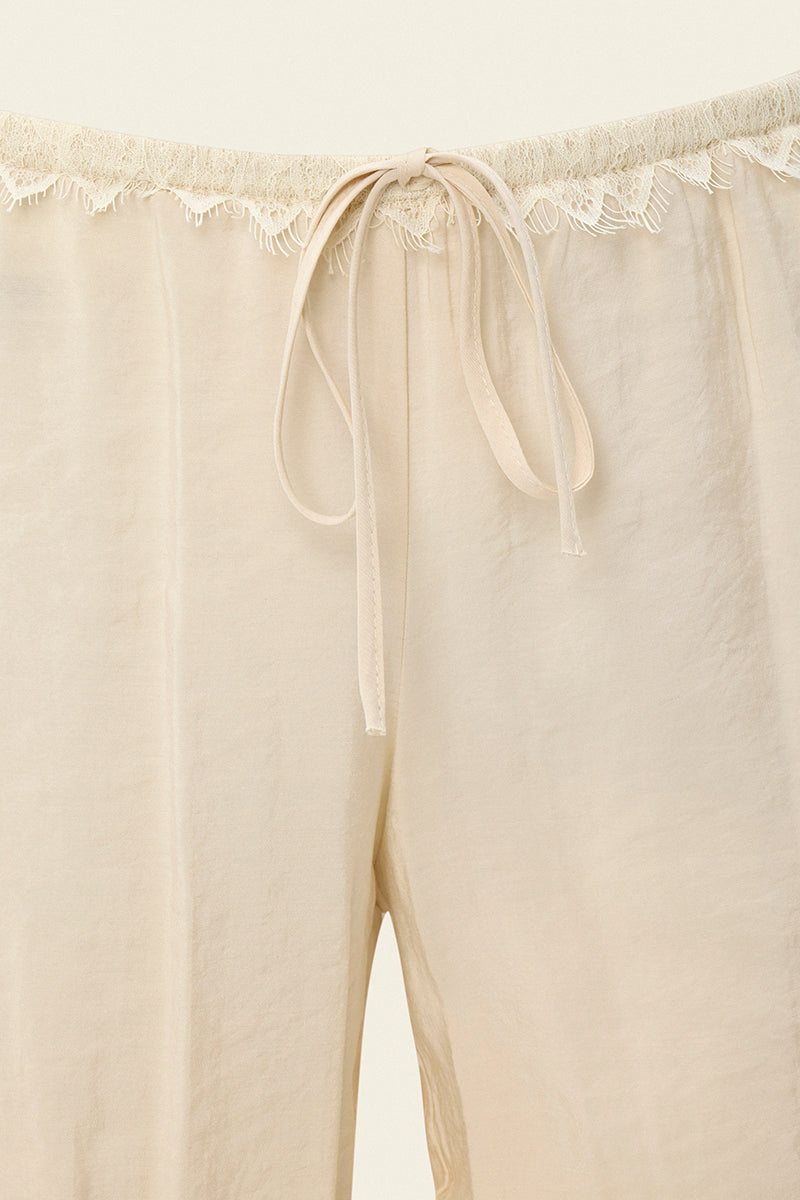 Cream Scylla pants by IKINITA, featuring a relaxed fit and stylish design, displayed on a model in a casual setting.