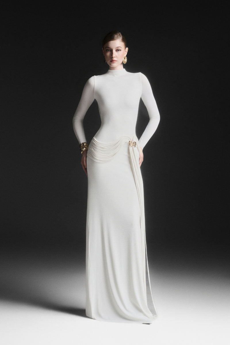 White Corvina draped floor-length gown by Maison Des Copains, elegant design with flowing fabric and sophisticated style.