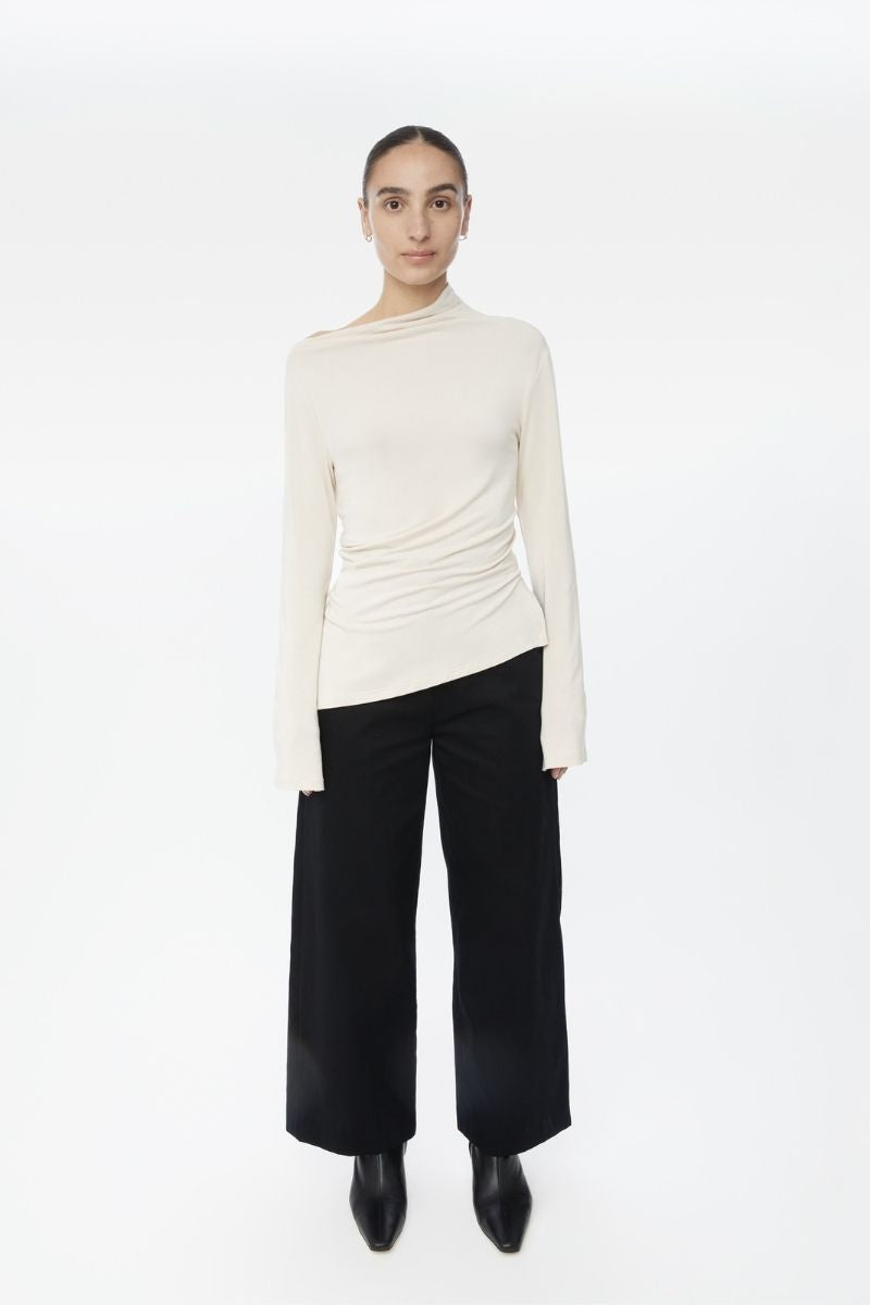Dāl the Label modal asymmetric knit top in neutral tones, featuring a stylish uneven hem and relaxed fit.