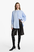 Acaria Studio iconic French blue shirt displayed on a hanger, showcasing its classic design and vibrant color.