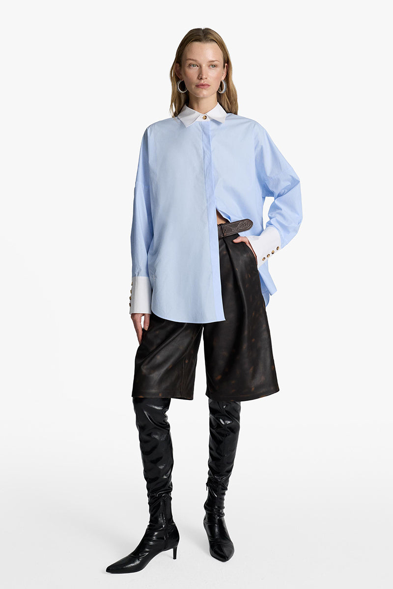 Acaria Studio iconic French blue shirt displayed on a hanger, showcasing its classic design and vibrant color.