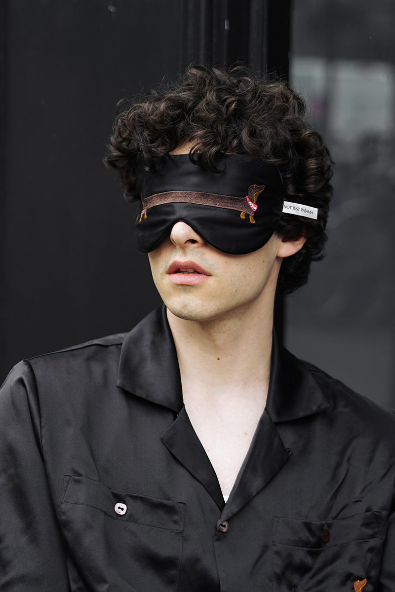 White silk sleeping eye mask featuring a dachshund design from Not Just Pajama, perfect for restful sleep.
