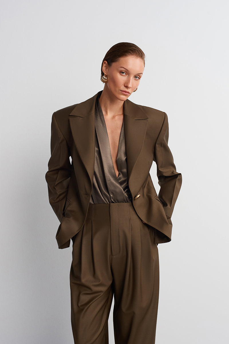 Acaria Studio Earth Blazer in hazelnut brown, tailored blazer with lapel collar and button closure, hanging on a wooden hanger.