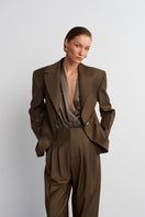 Acaria Studio Earth Blazer in hazelnut brown, tailored blazer with lapel collar and button closure, hanging on a wooden hanger.