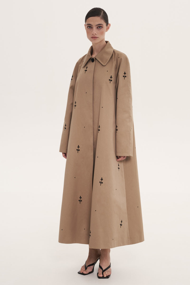 Beige rose embroidered trench coat by DELEGAN, showing detailed floral embroidery and classic coat design.