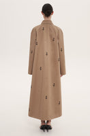 Beige rose embroidered trench coat by Delegan displayed on a hanger with detailed floral embroidery and classic design.