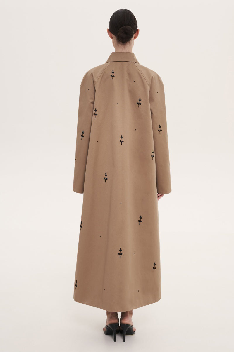 Beige rose embroidered trench coat by Delegan displayed on a hanger with detailed floral embroidery and classic design.
