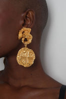 Anatina medallion earrings featuring circular gold-tone charms with intricate engraved details, hanging from delicate hooks.