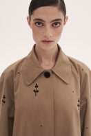Beige rose embroidered trench coat by DELEGAN, featuring intricate embroidery and classic design, displayed on a hanger.