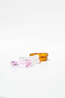 Set of three SALVÁREA Remolino rings in pink, amber, and white, featuring unique swirling designs on smooth metal bands.