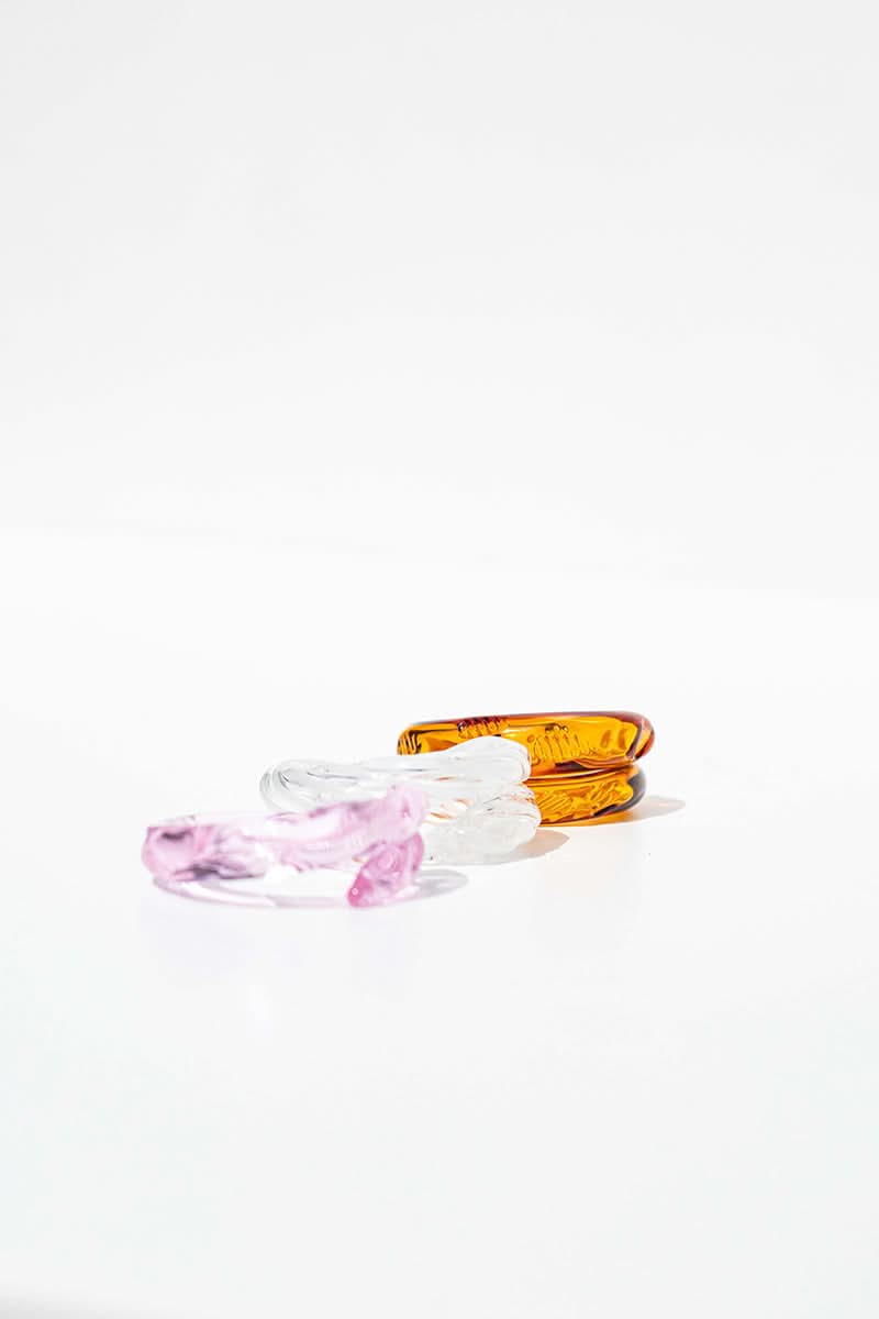 Set of three SALVÁREA Remolino rings in pink, amber, and white, featuring unique swirling designs on smooth metal bands.