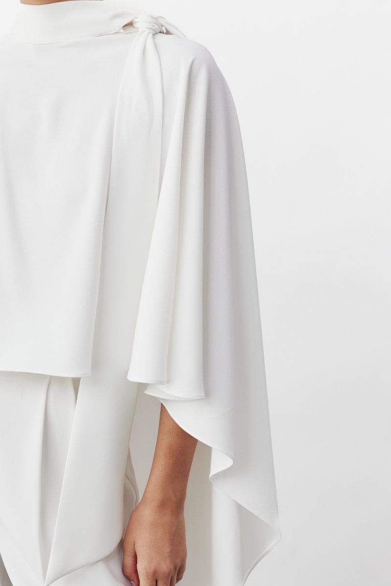 White Caro Crepe Cape jacket by Nazlı Ceren, shown draped over a mannequin, highlighting its elegant, flowing fabric and stylish design.