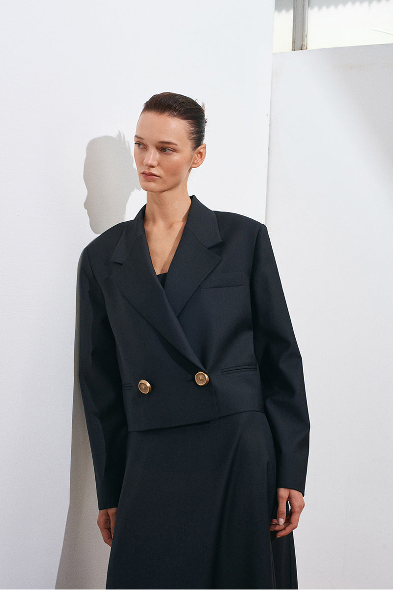 Black Guru crop blazer by Acaria Studio, shown on a hanger, featuring a fitted design with structured lapels and long sleeves.