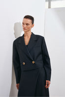 Black Guru crop blazer by Acaria Studio, shown on a hanger, featuring a fitted design with structured lapels and long sleeves.