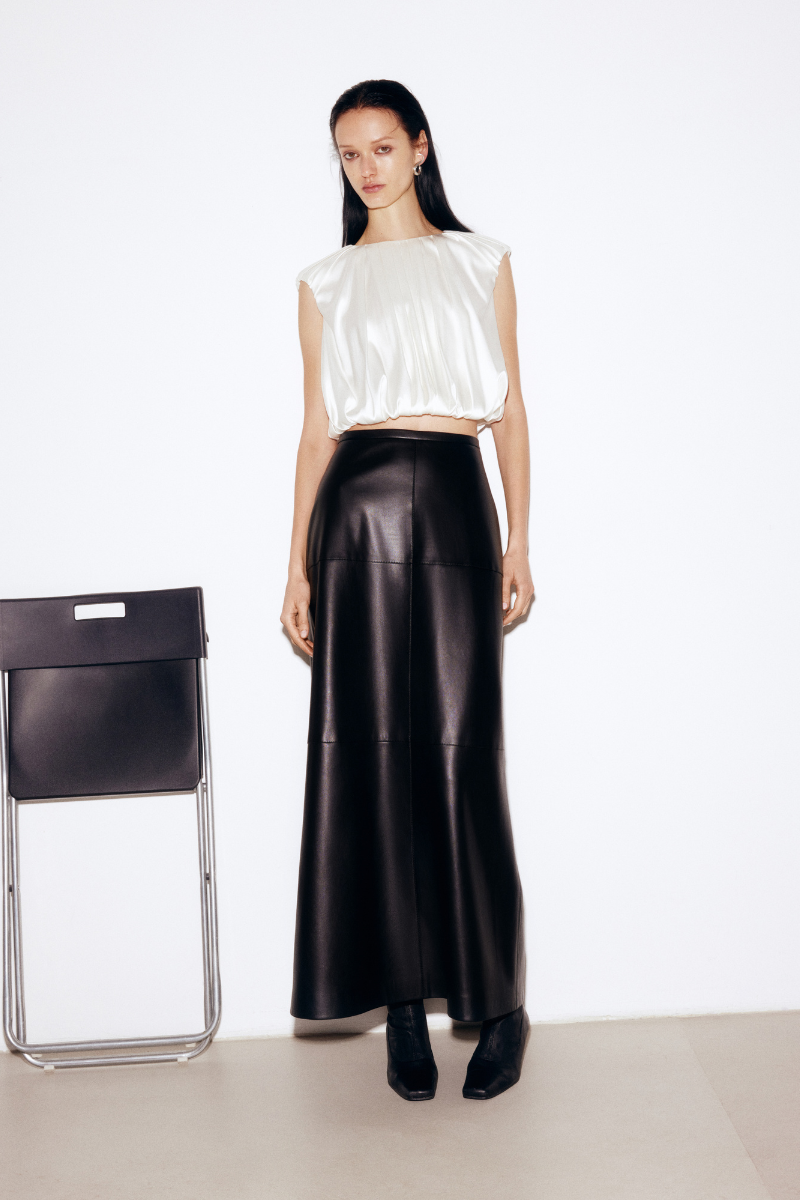 Black faux leather midi skirt by ELENAREVA featuring a fitted waist and sleek, modern design, shown on a model.