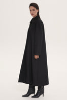 Black trench coat by Delegan hanging on a wooden hanger, showcasing its classic design and tailored fit.