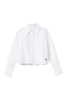 Dāl the Label cropped cotton button-down shirt with long sleeves and a classic collar, shown in a natural fabric texture.