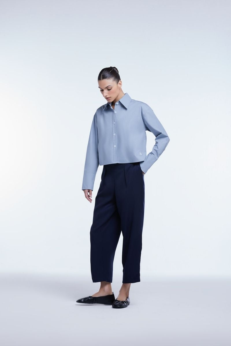 Dāl the Label cropped cotton button-down shirt in white, featuring a classic collar and long sleeves, displayed on a hanger.
