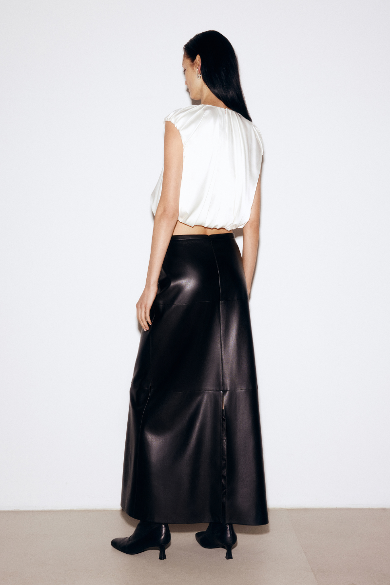 Black faux leather midi skirt by ELENAREVA, shown on a model with a high waist and sleek, fitted design.