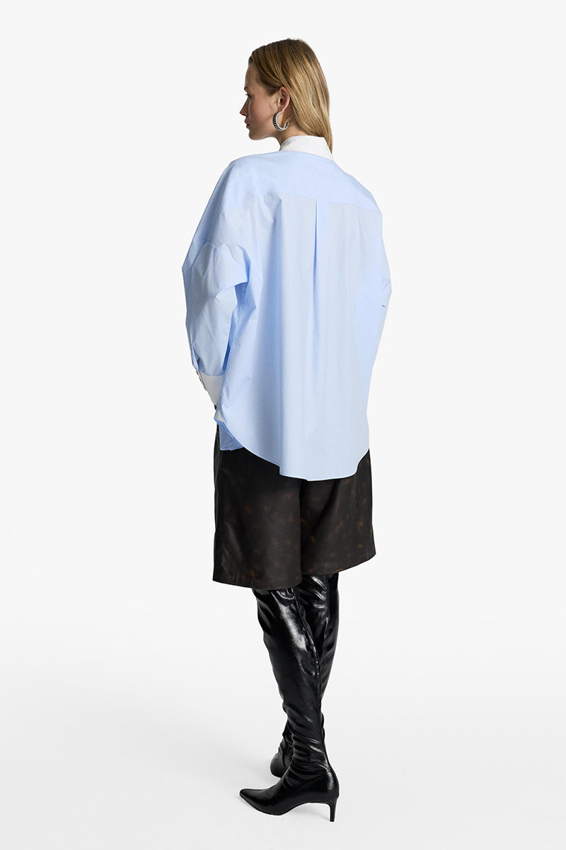 Acaria Studio iconic French Blue shirt with a classic fit, featuring a collar and button-down front, displayed on a hanger.