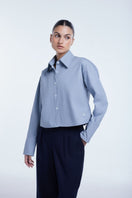 Dāl the Label cropped cotton button-down shirt in white with long sleeves and a classic collar, styled on a mannequin.