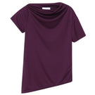 Dāl the Label asymmetrical short sleeve top with a unique uneven hem and relaxed fit, styled in a casual indoor setting.