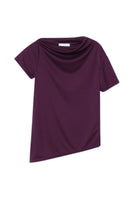 Dāl the Label asymmetrical short sleeve top with a unique uneven hem and relaxed fit, styled in a casual indoor setting.
