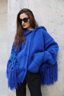 Blikvanger fringed poncho-style cardigan with tassel details, cozy knit fabric, and relaxed fit, draped over a mannequin.