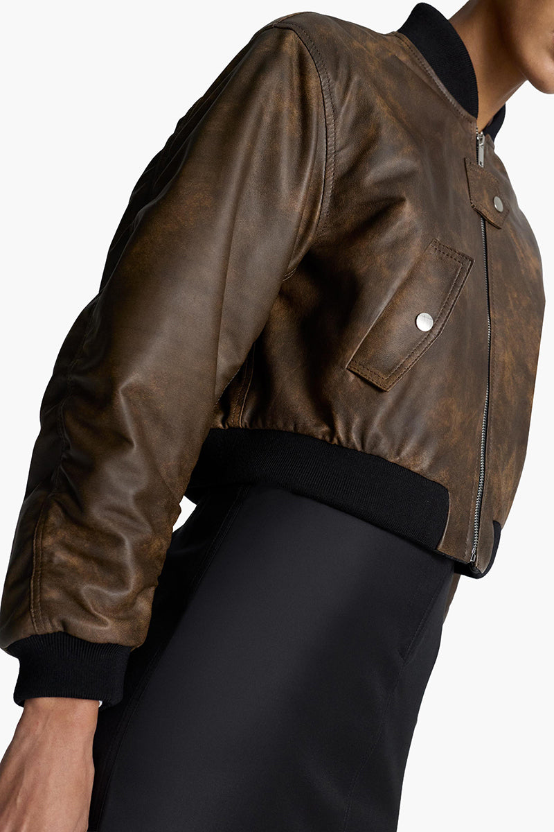 Acaria Studio Nostalgie leather bomber jacket with classic design, brown leather, and ribbed cuffs, displayed on a hanger.