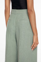 Light beige linen wide-leg pants by Dāl the Label hanging on a wooden hanger, showcasing relaxed fit and breathable fabric.